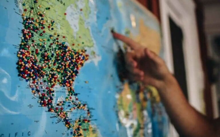 Hand pointing to a map of the United States with hundreds of pins in it