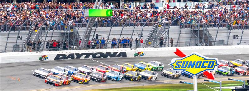 view of nascar stock cars on the daytona 500 international speedway track with crowd in the background and sunoco loge in the front